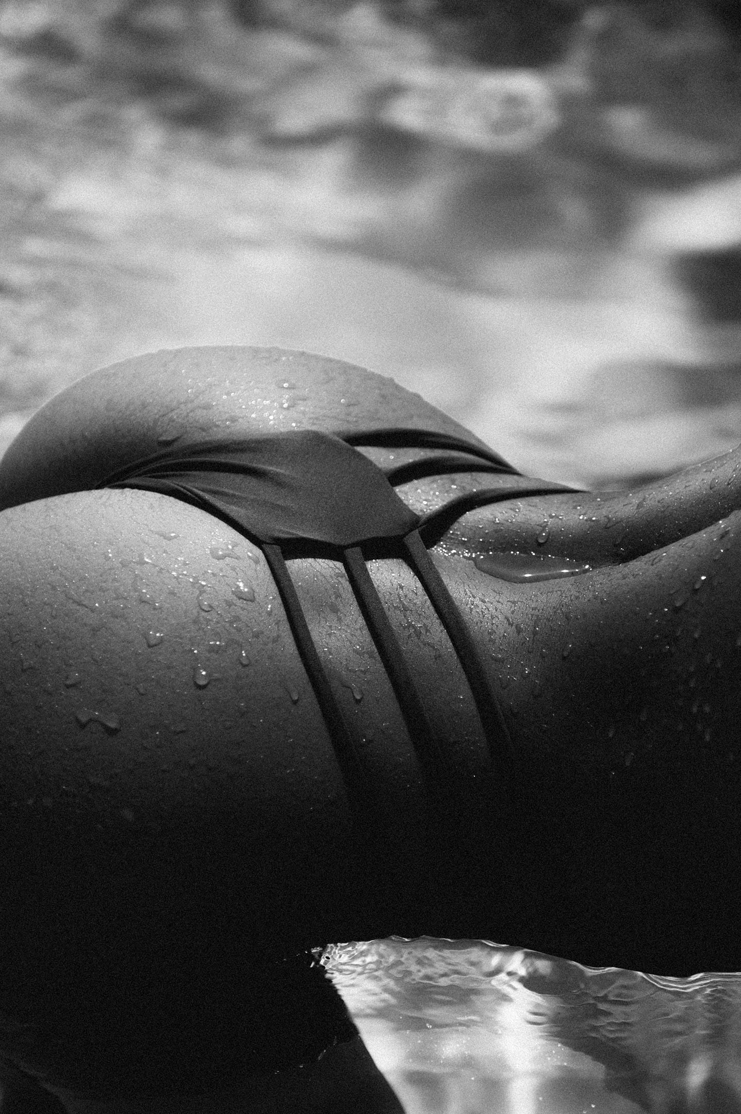 Close detail of water droplets on skin and swimwear at the waterline, photographed by Tatyana Kudryashova.