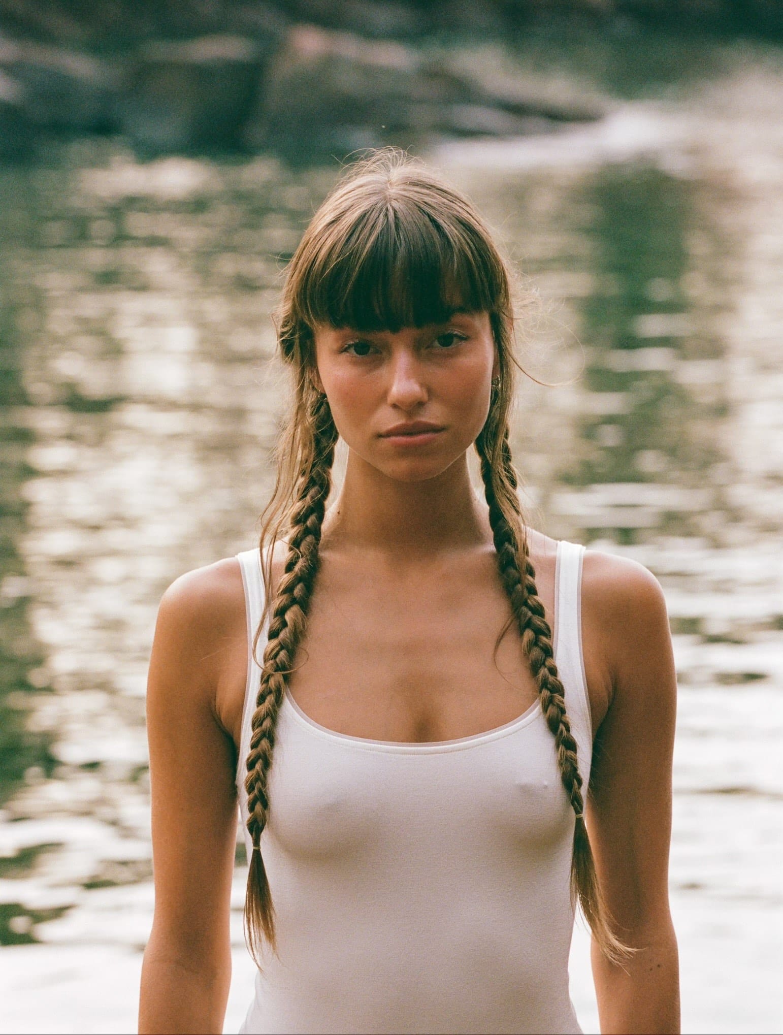 Close portrait of Telma Louise standing in front of water with braids over her shoulders and chest in a wet white one-piece, photographed by Anna Klembarova.