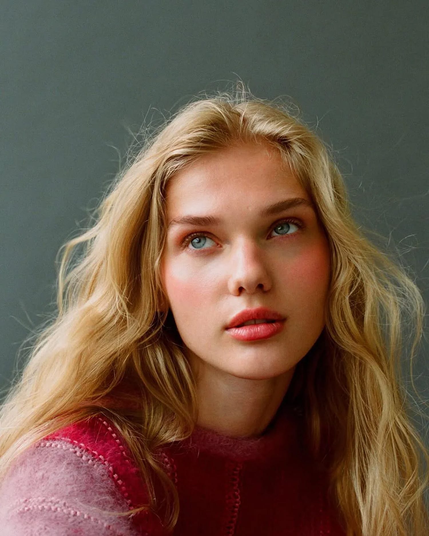 Close portrait of Vasilina Kireenko looking upward in a pink mohair sweater, soft light on her face, photographed by Sasha Tsyganok.