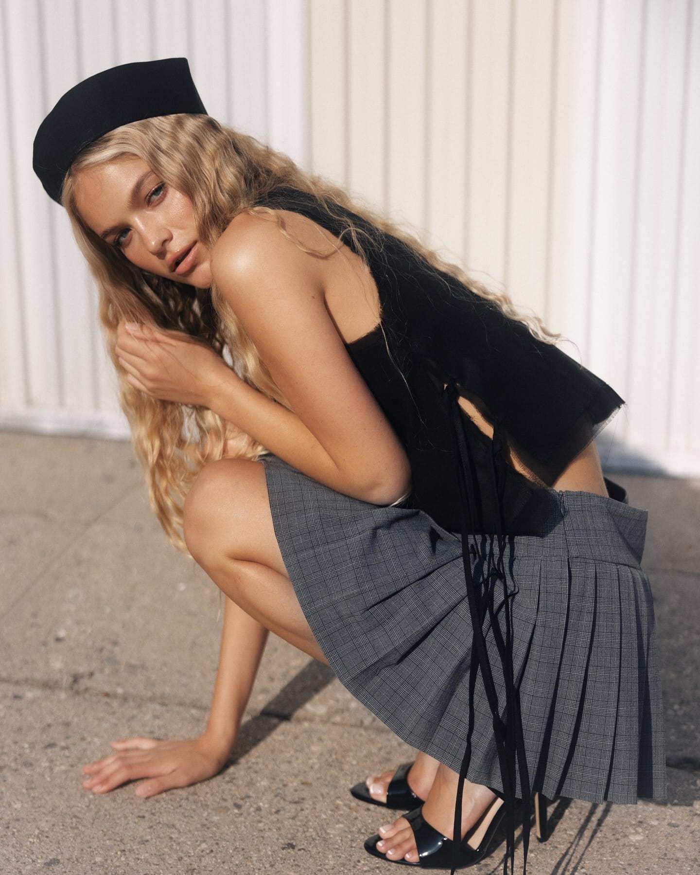 Cadence van Hoften crouches on pavement in a black fringed top and grey check skirt, blonde hair falling forward, photographed by Olga Aleshina.