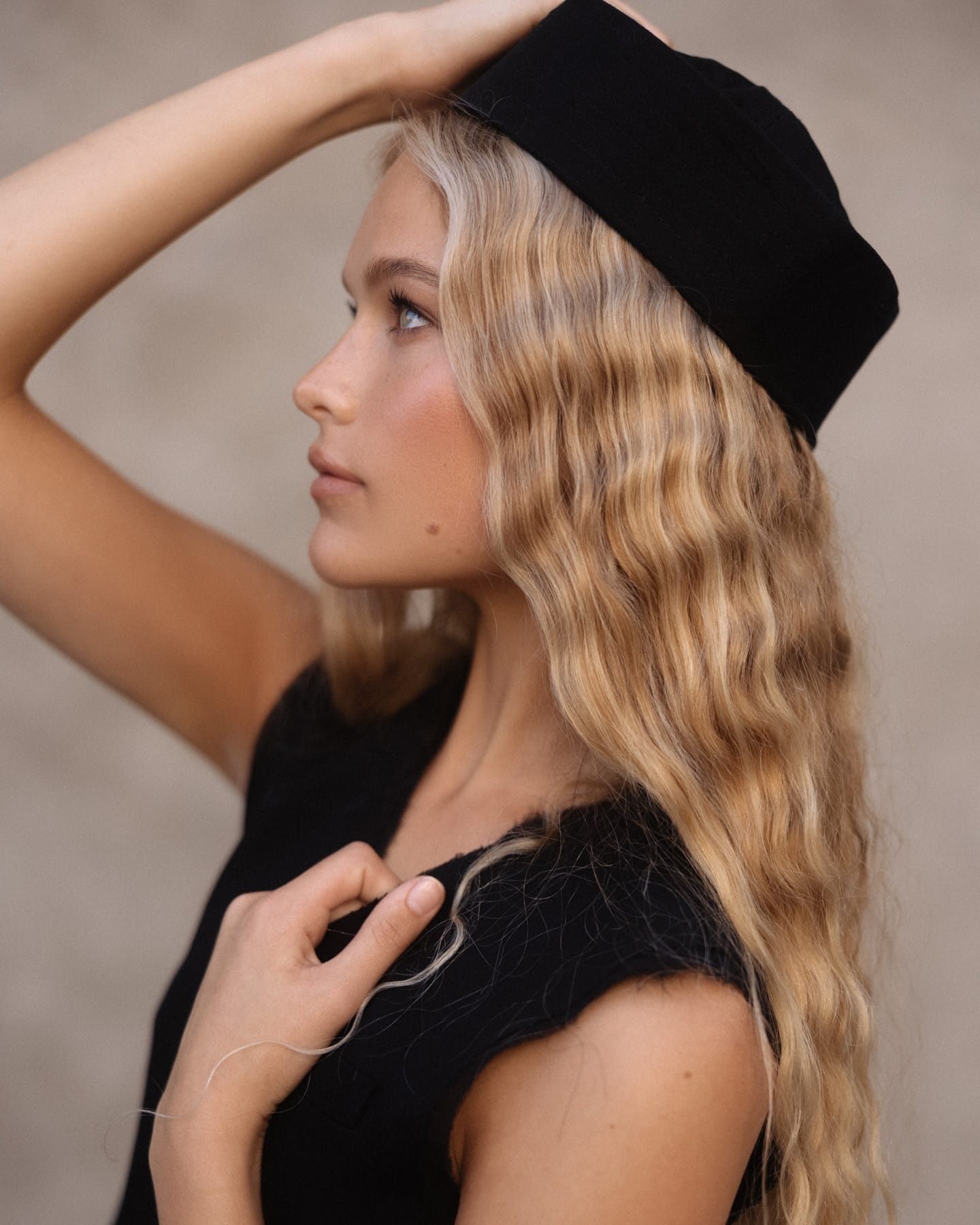Profile portrait of Cadence van Hoften adjusting her pillbox hat in a black textured top, photographed by Olga Aleshina.