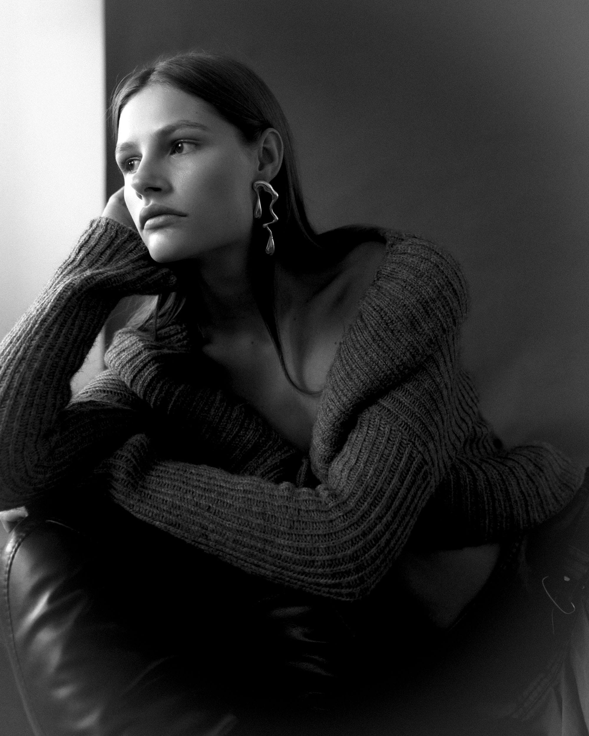 Close portrait of Eva Shevkoplyas wrapped in a ribbed cardigan with a sculptural earring, looking toward the window, photographed by Olesya Skvortsova.