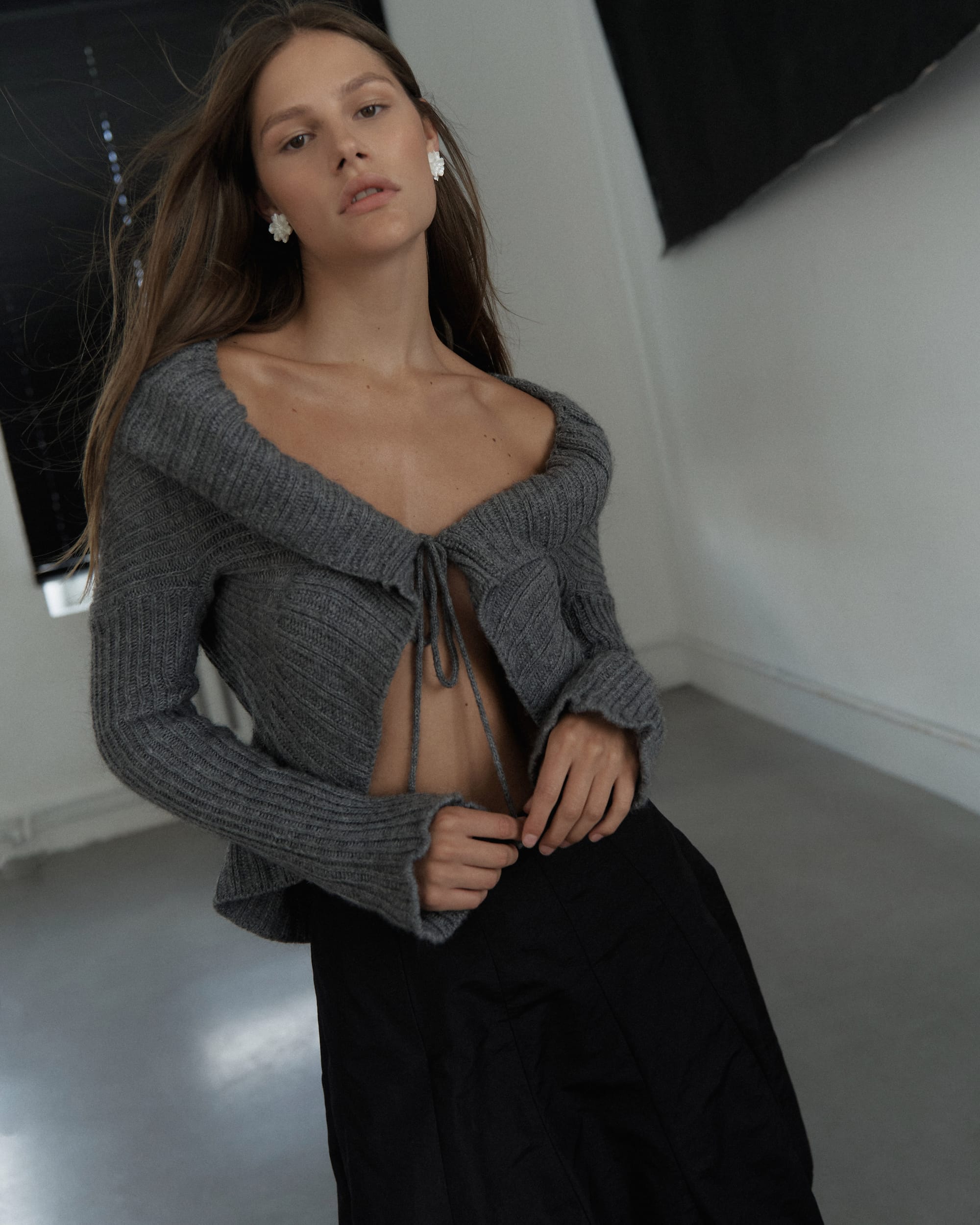 Eva Shevkoplyas in a grey tie-front cardigan and black skirt with cluster earrings, shot from below, photographed by Olesya Skvortsova.