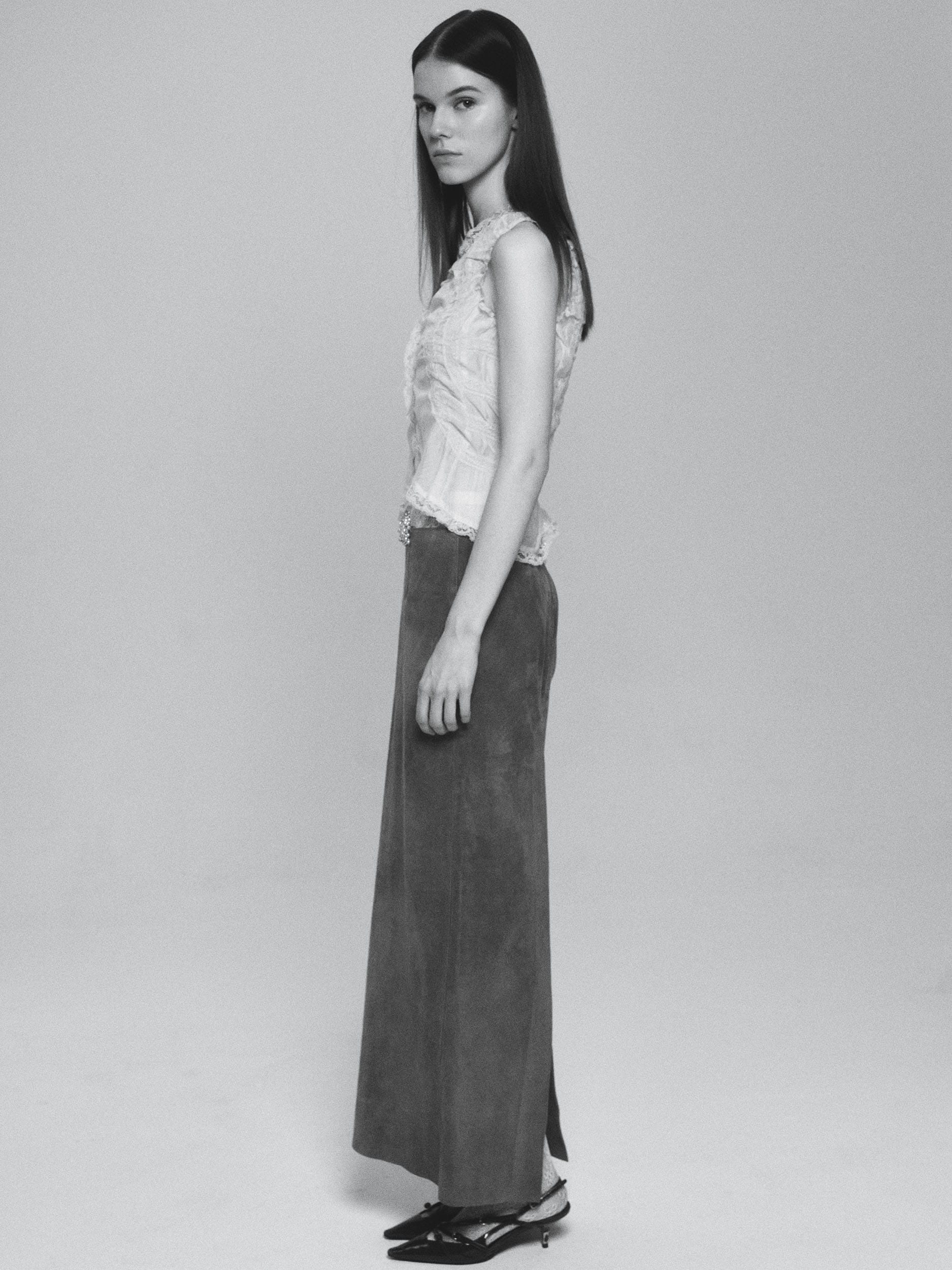 Greta Dethlefs in profile in a lace top and long suede skirt with kitten heels, black and white, photographed by Pascal Bräuer.
