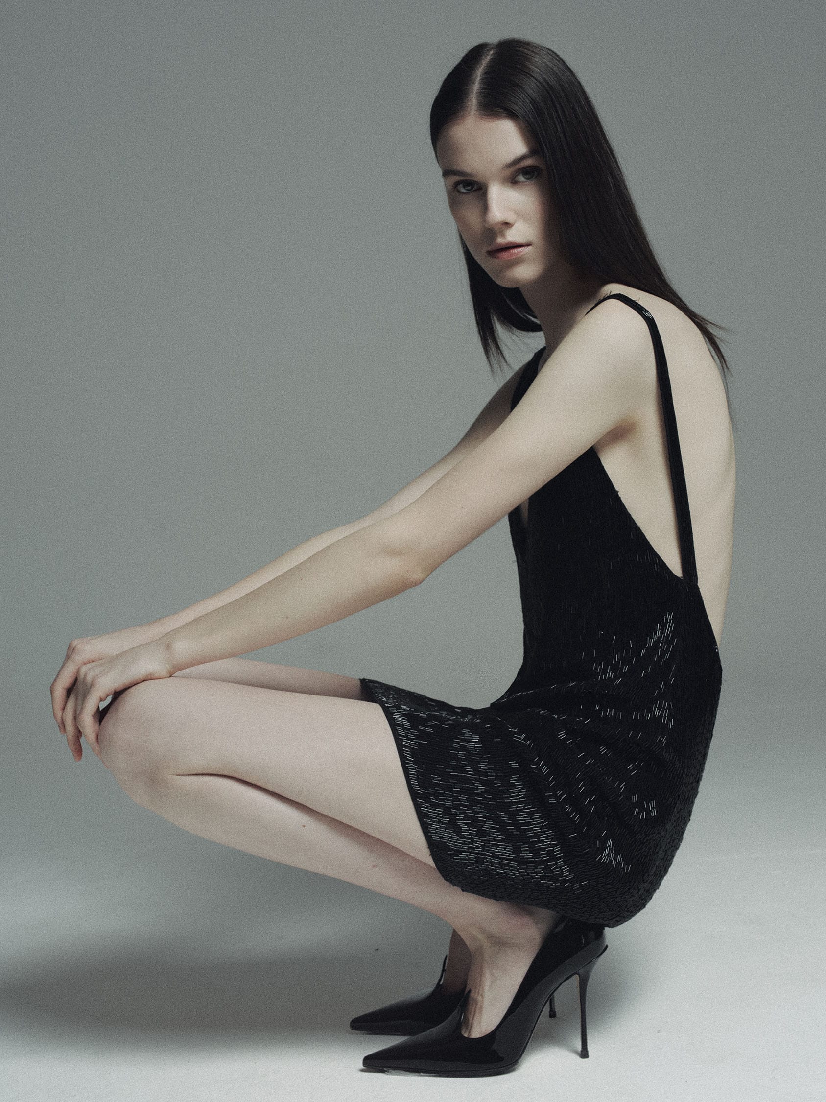 Greta Dethlefs crouches in a beaded black mini dress and patent stilettos, looking into the lens, photographed by Pascal Bräuer.