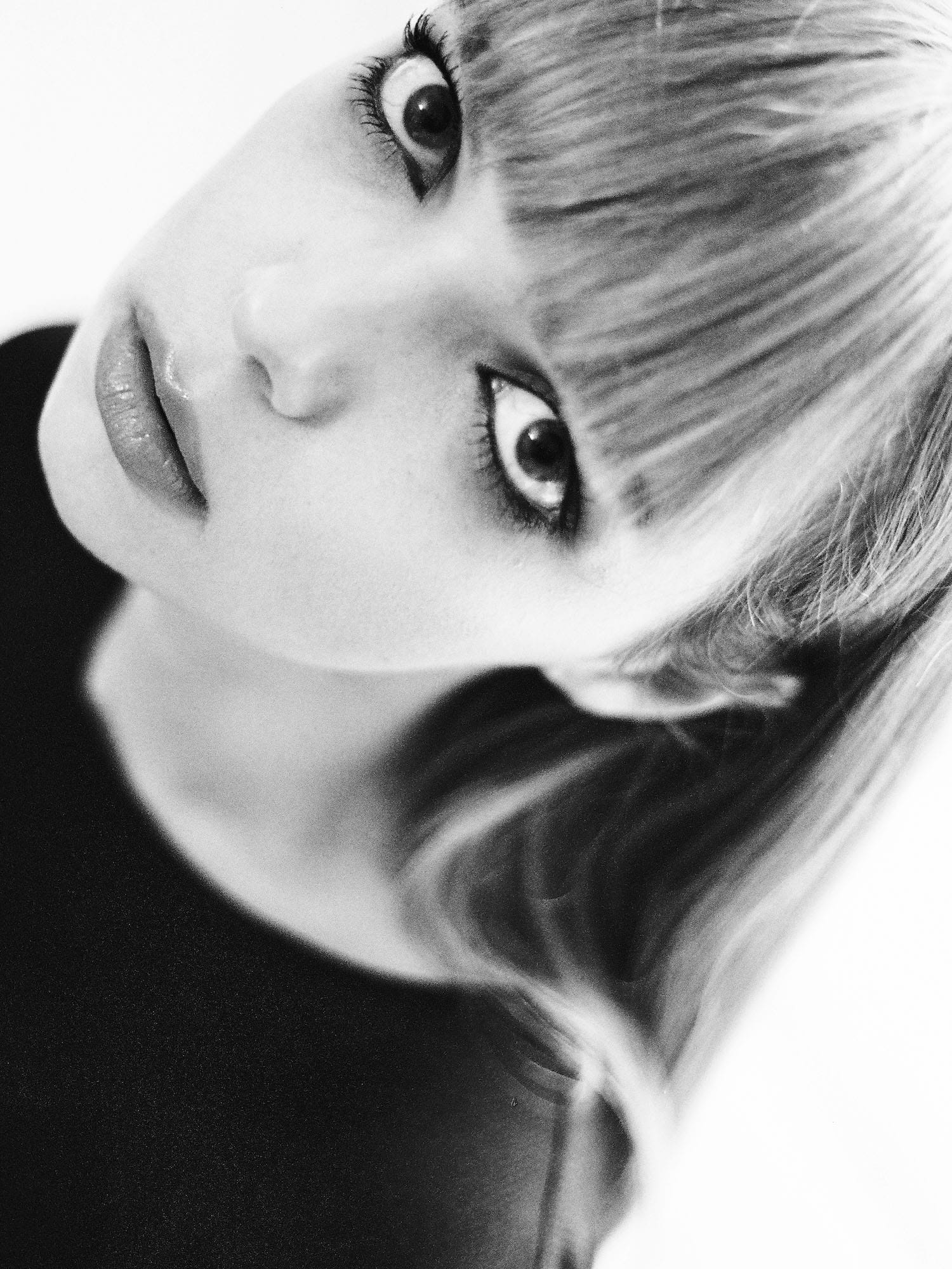 Tilted close-up of Mari Marchenkova's face in black and white, blonde bob falling across her forehead, photographed by Anna Verkhoumova.