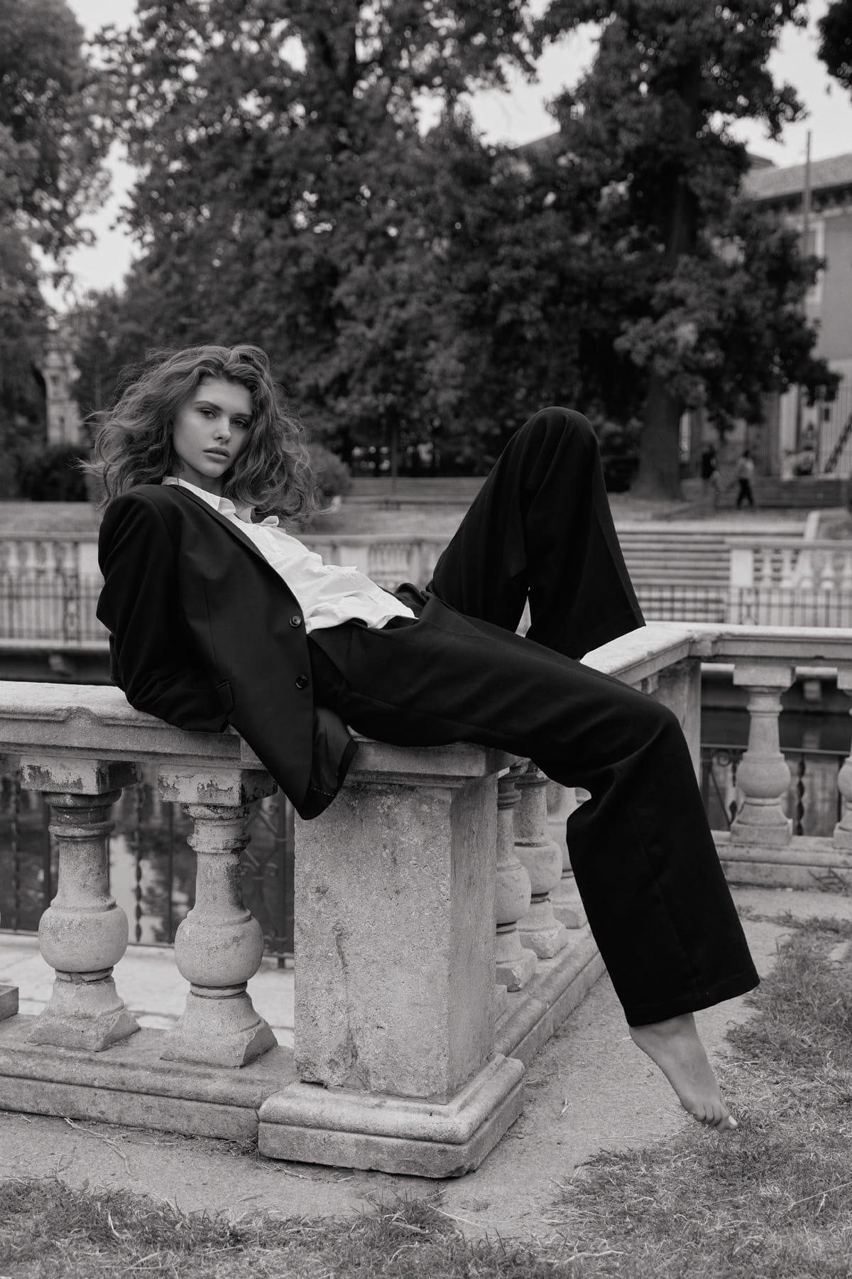 Alyona Lihosherstowa reclines on a marble balustrade with one bare foot extended, the suit jacket open over a white shirt, photographed by Alexei Bazdarev.