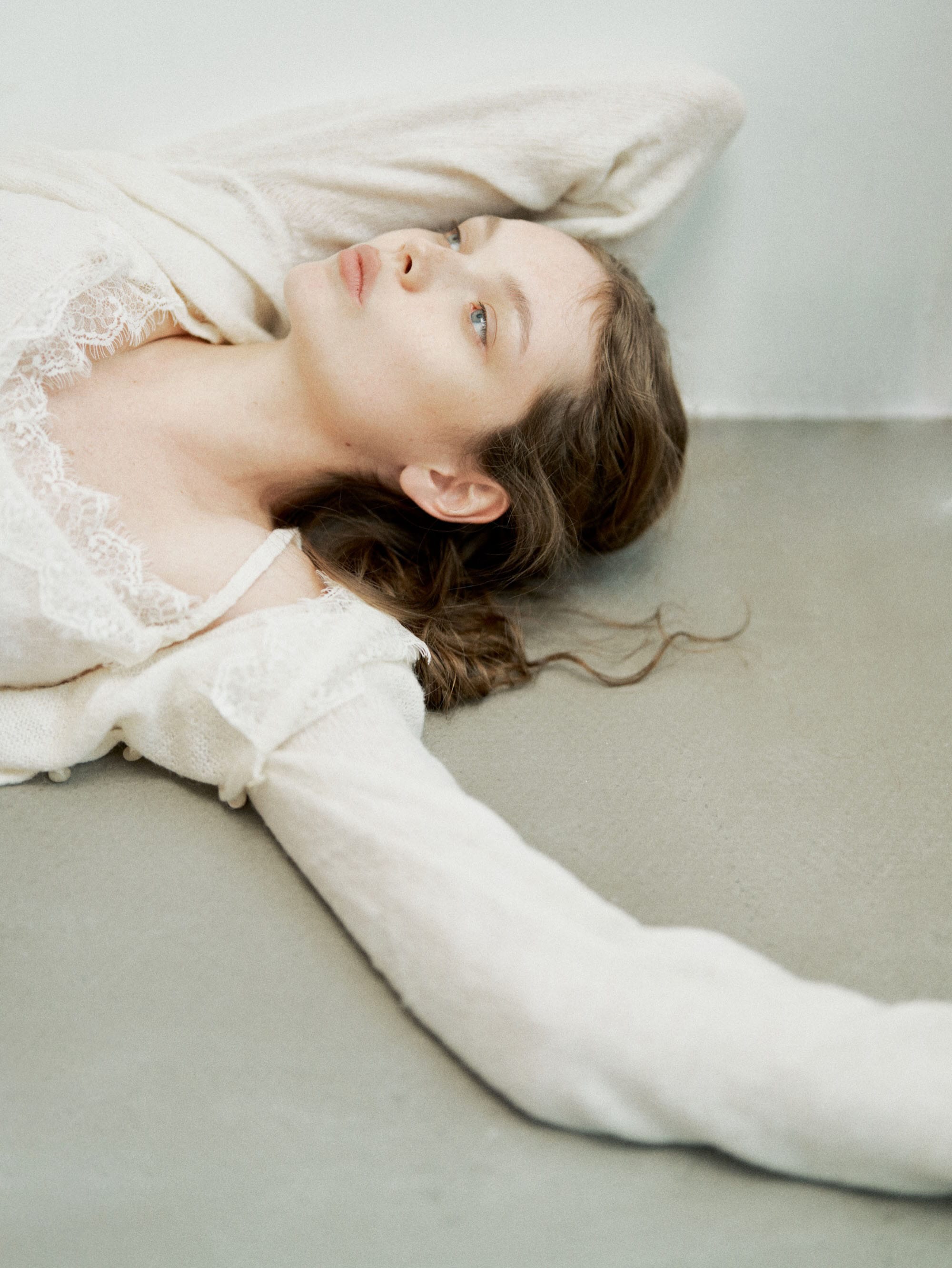 Anna lies on her back with her hair fanned across the floor, looking up, in a lace-trimmed camisole and cream cardigan, photographed by Svetlana Latyshko.