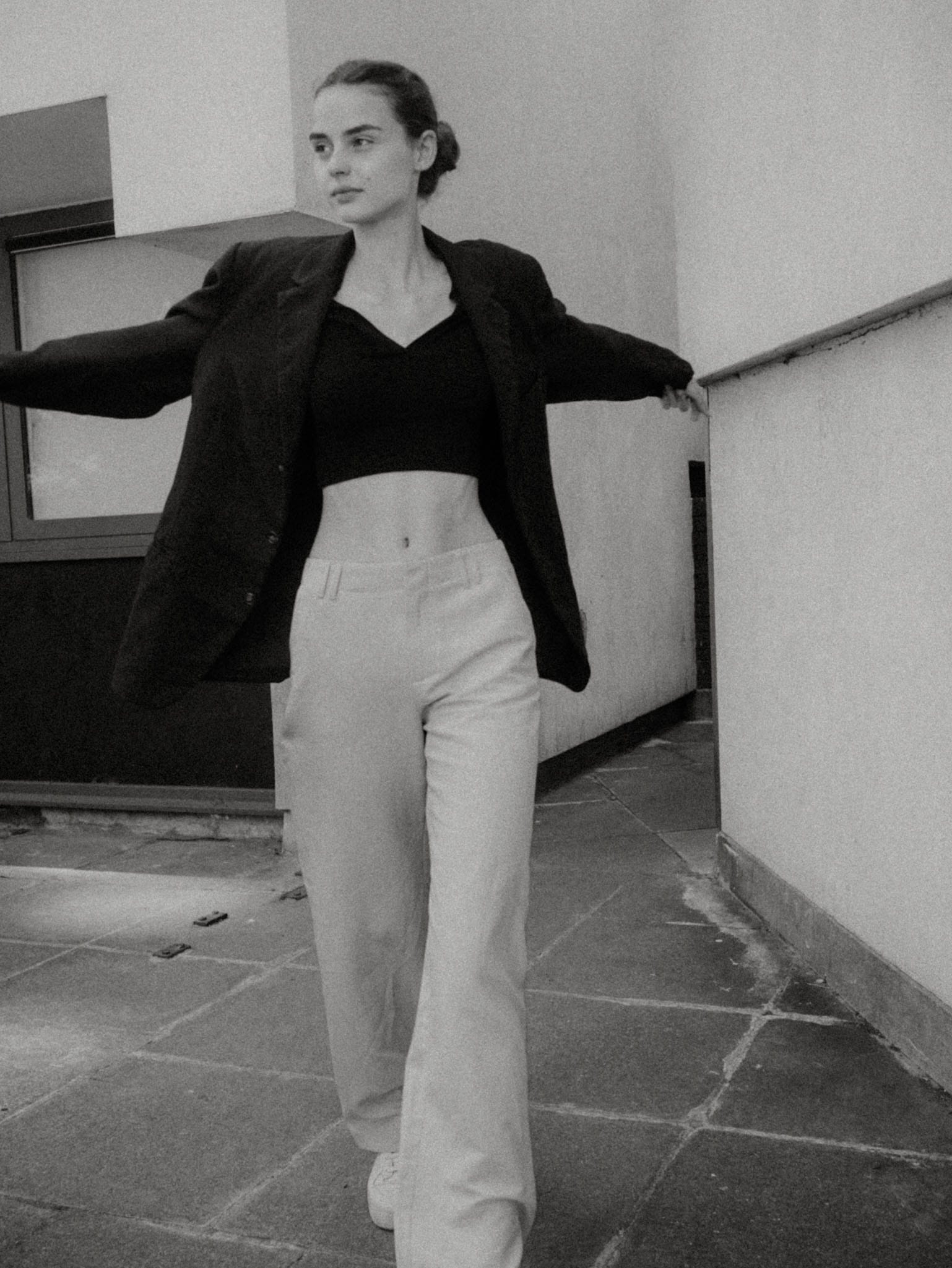 Giulia Bonatesta walks through a tiled passageway in a cropped black polo, blazer and cream trousers, photographed by Charles Cave.
