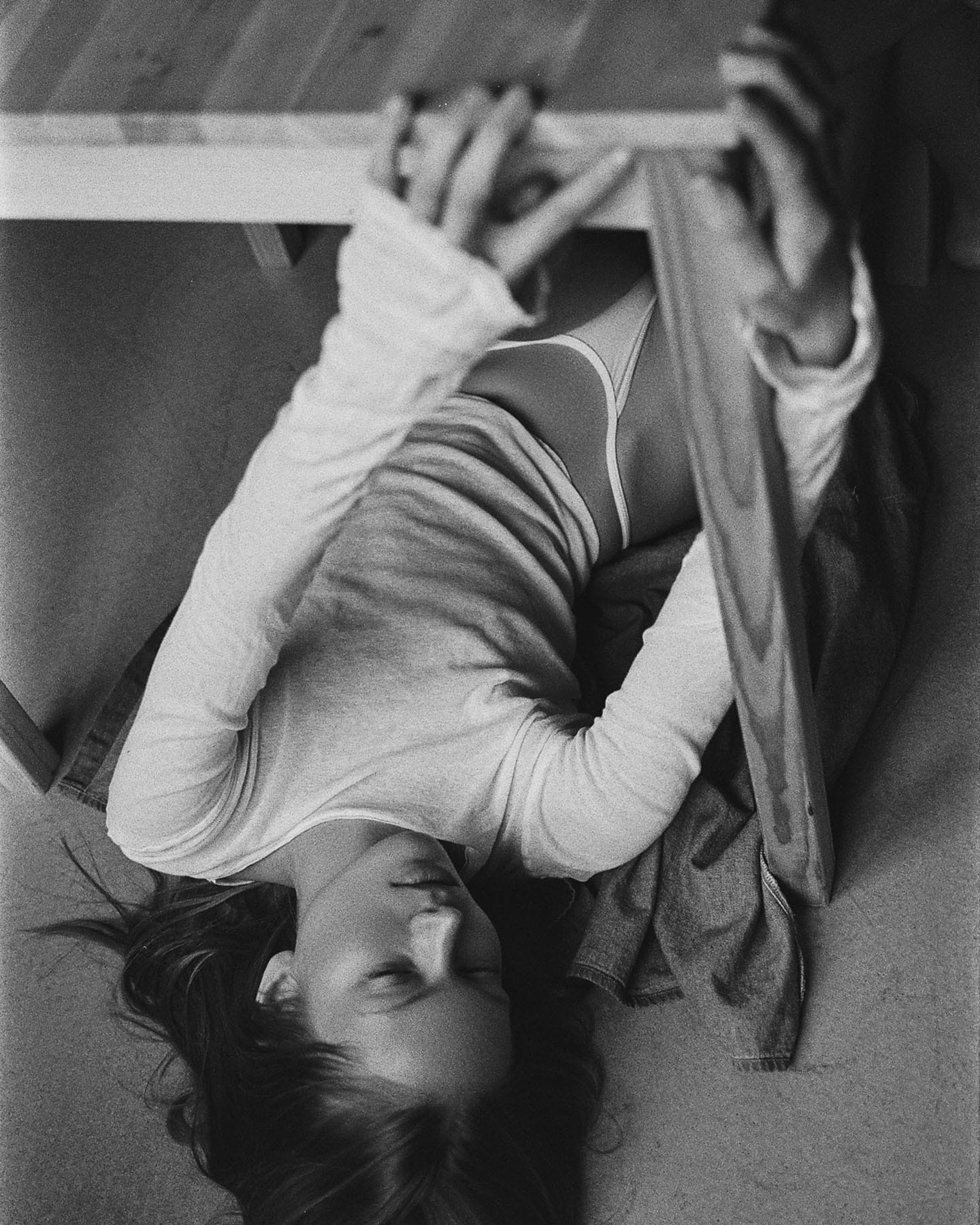 Maria Privalova lies on her back, head tipped toward the camera, gripping a wooden table leg overhead, by Natasha Skatnikova.