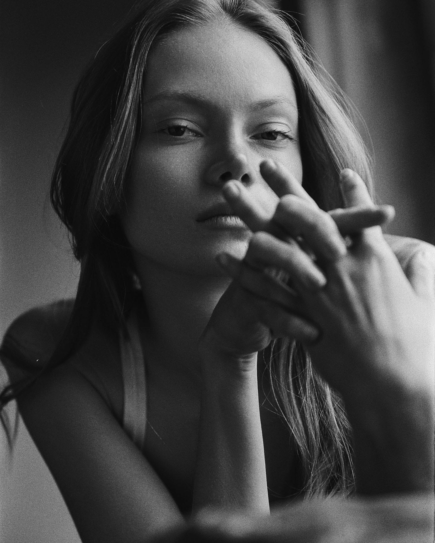 Maria Privalova holds her interlaced hands before her face, hair loose, maintaining eye contact, by Natasha Skatnikova.