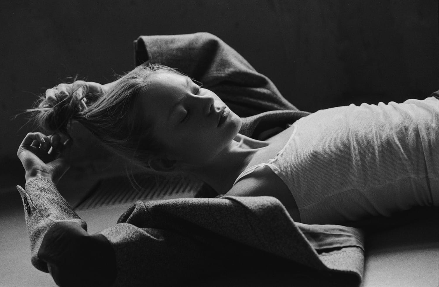 Maria Privalova lies back on the floor by a radiator, eyes closed, hands in her hair, in a tank and open jacket, by Natasha Skatnikova.