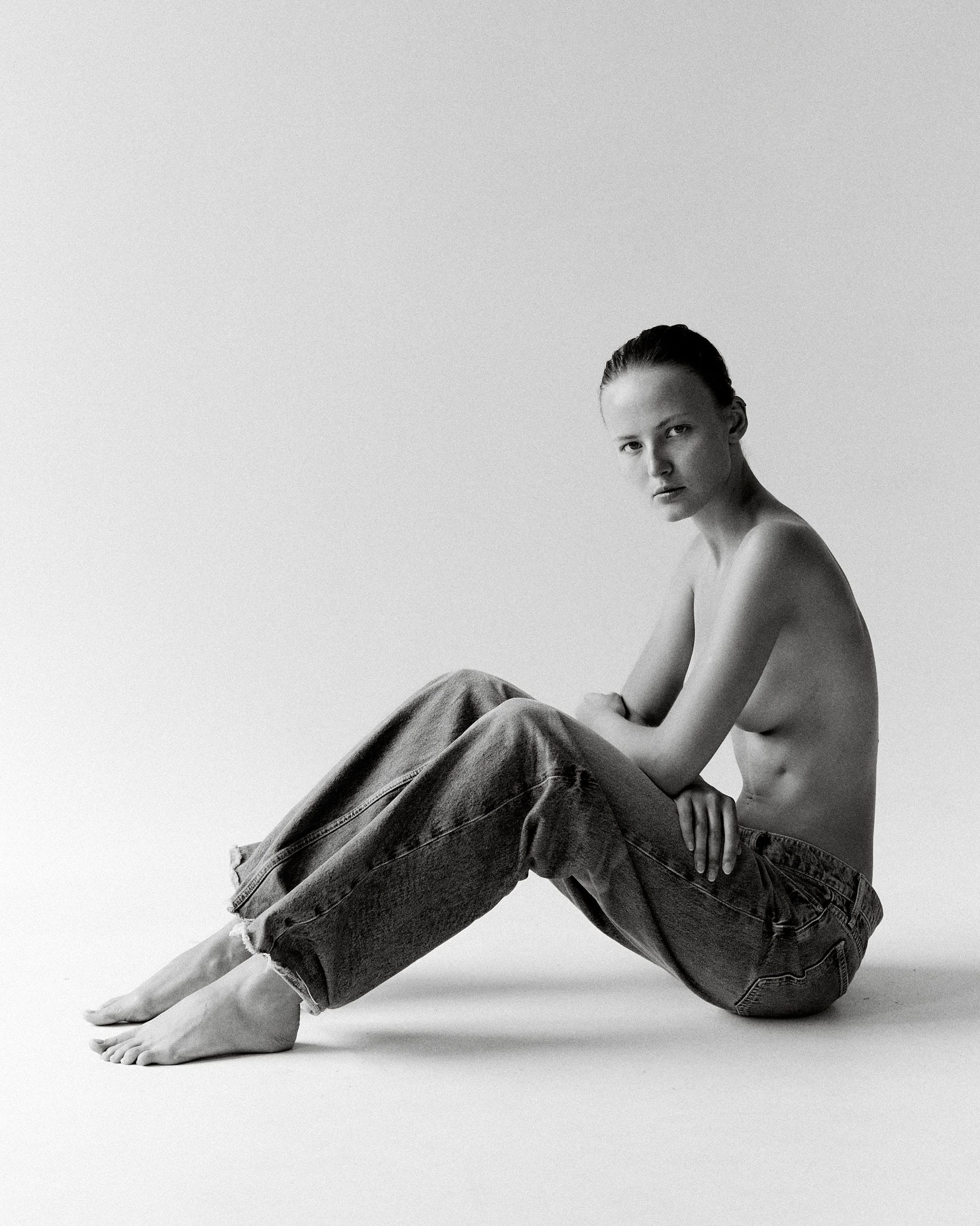 Tanya Korné sits on the floor in profile with her knees drawn up, arms resting on her lap, looking back at the lens, photographed by Darya Abramova.