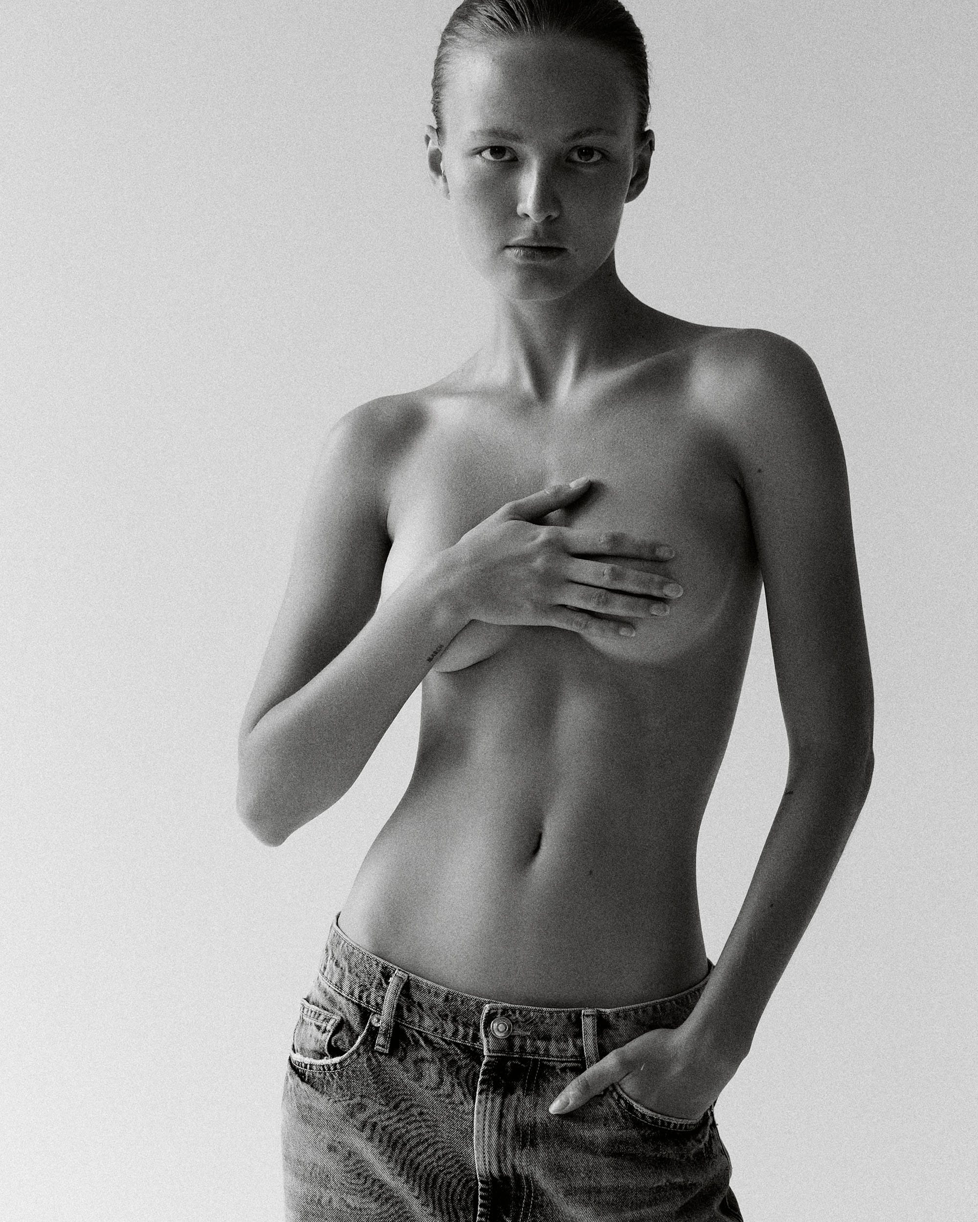 Tanya Korné stands topless in faded denim with one hand cupped over her chest, looking straight into the lens, photographed by Darya Abramova.