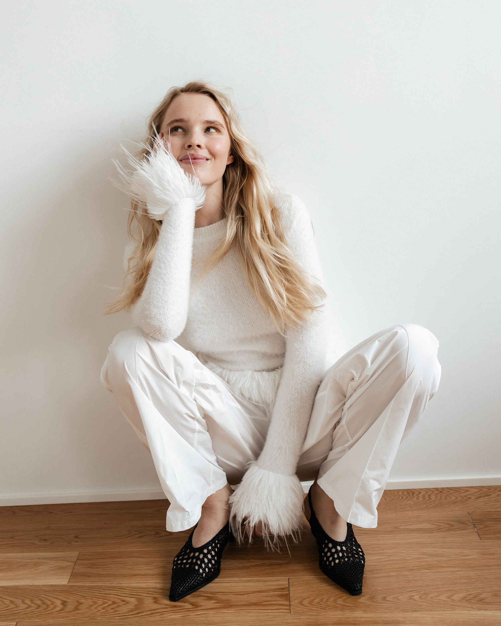 Jeanne Markevich in a feather-trim sweater and white pants, hand at her cheek, by Kristina Ranneva.