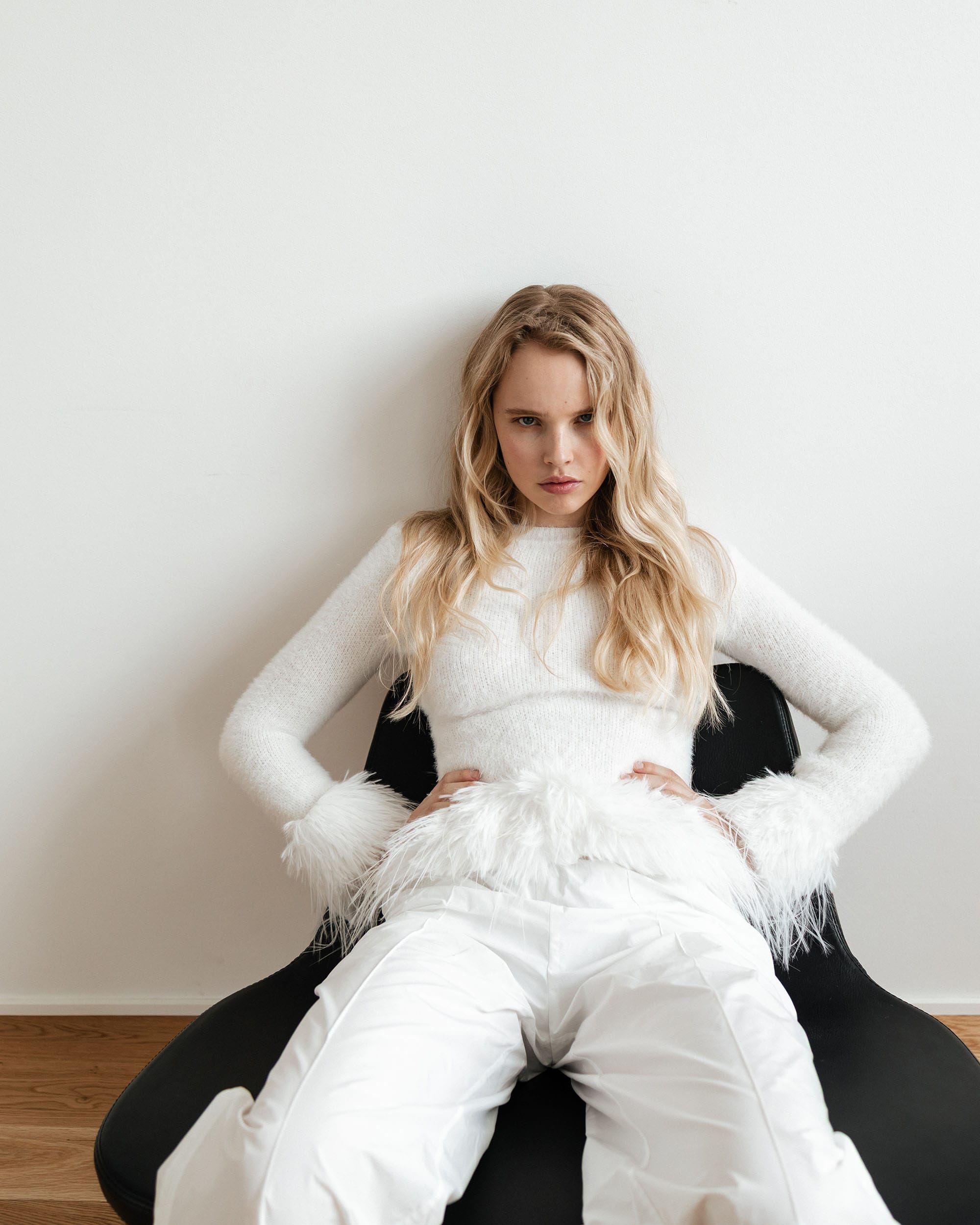 Jeanne Markevich sits in a feather-trim sweater and white pants, hands at her hips, by Kristina Ranneva.