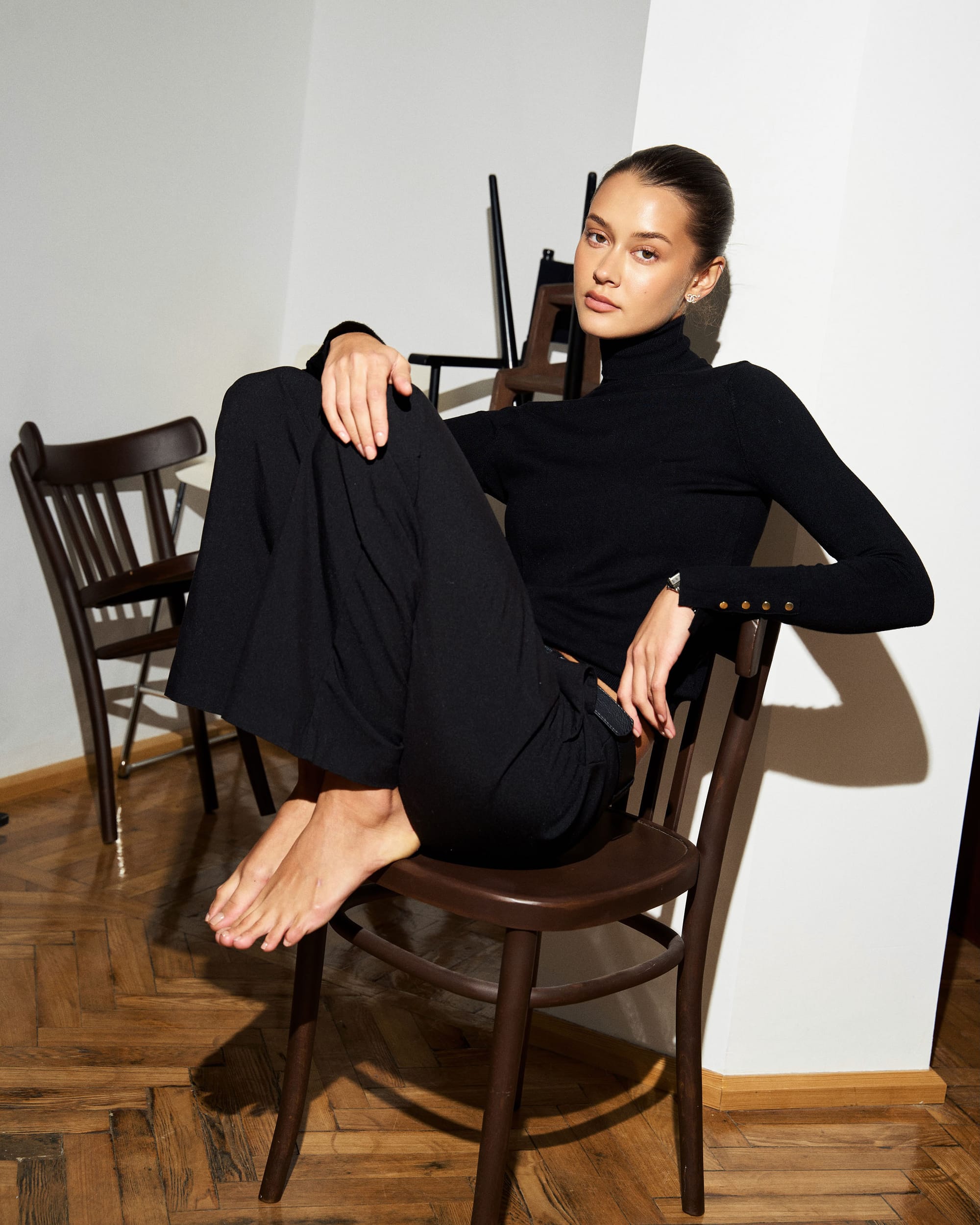Kristina Yakovleva sits on a bentwood chair in a black turtleneck and trousers, both feet up, by Maxim Kabanov.
