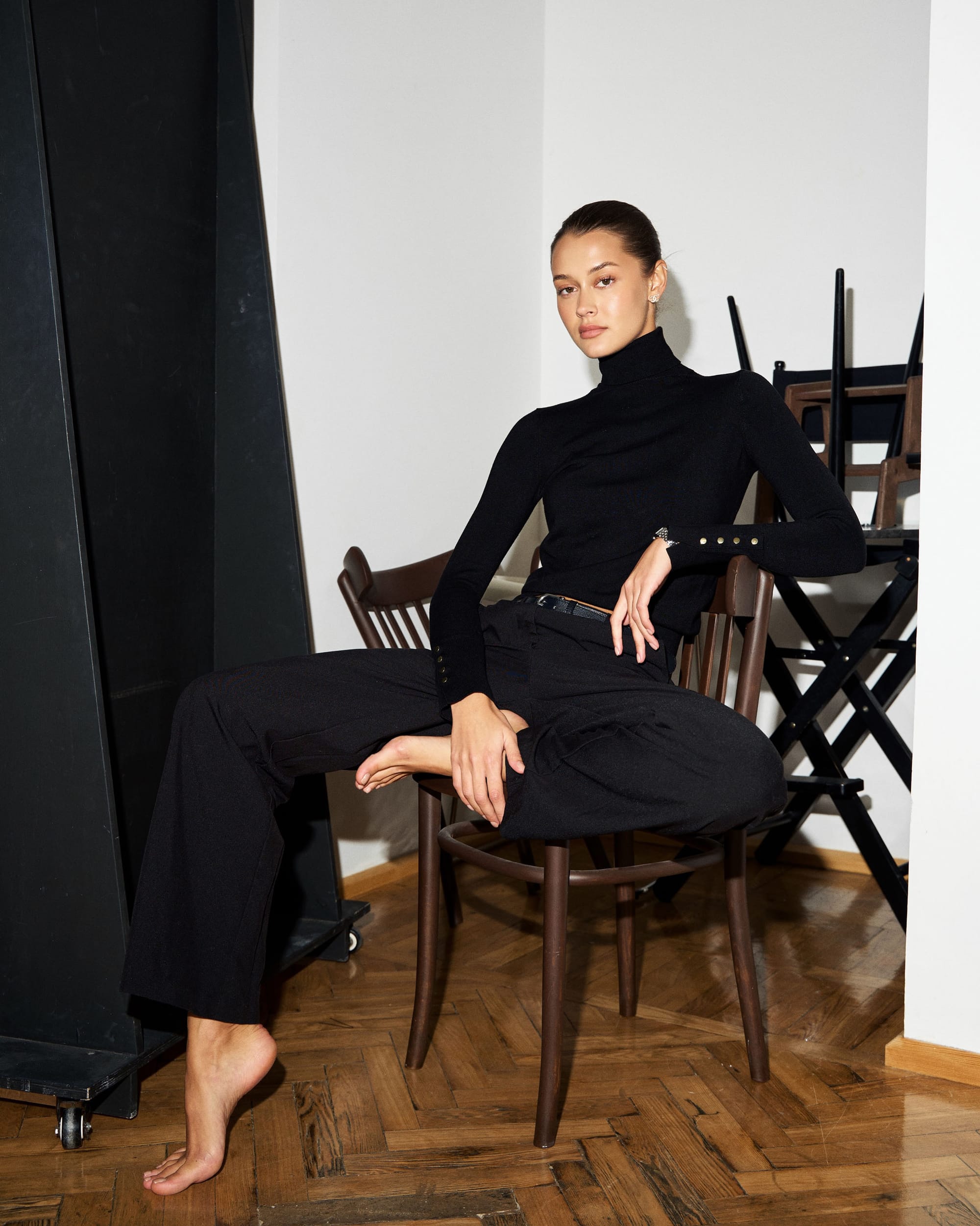 Kristina Yakovleva sits on a bentwood chair with one leg crossed over the other, in all black, by Maxim Kabanov.