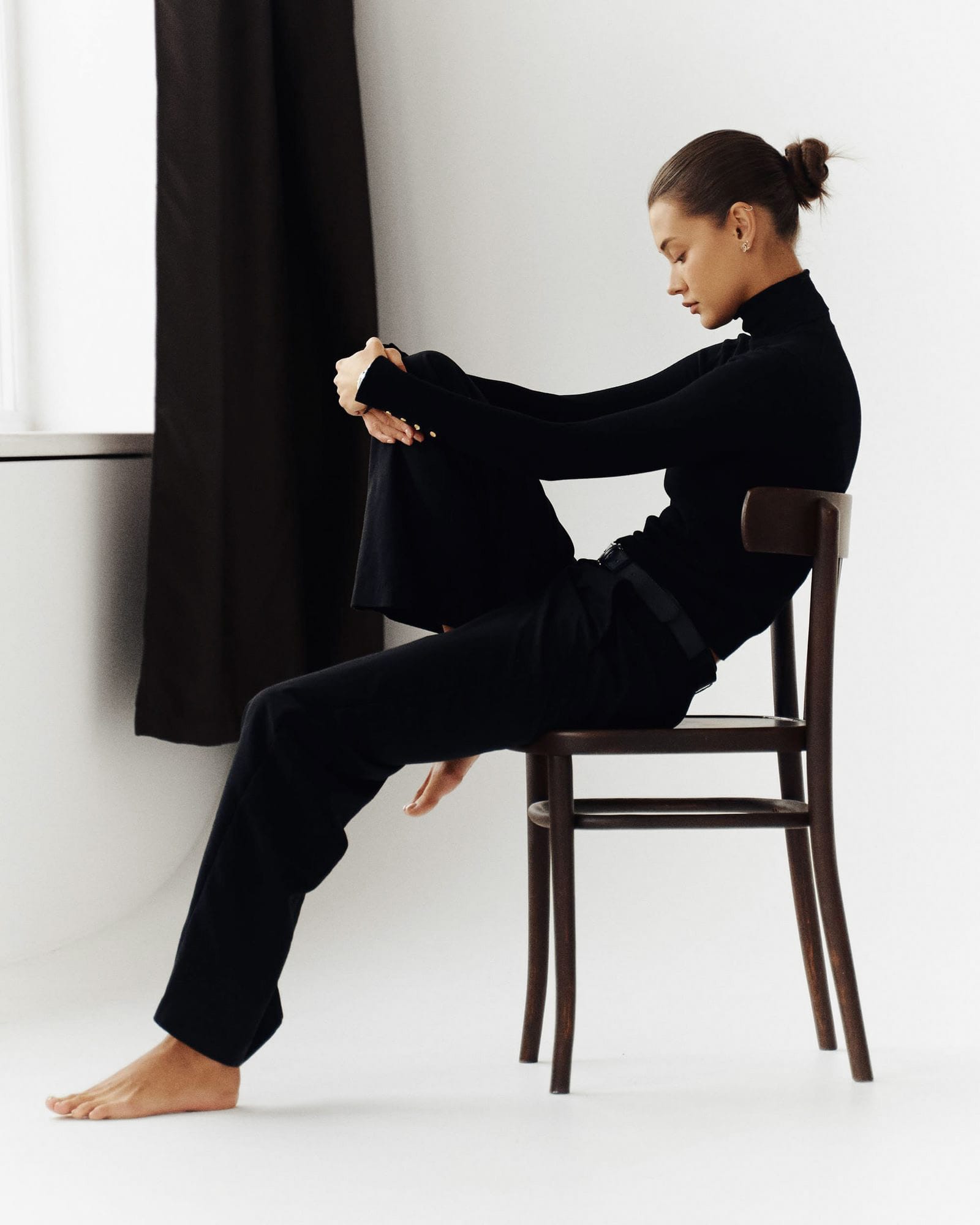 Kristina Yakovleva sits in profile on a bentwood chair in all black with her head bowed, by Maxim Kabanov.