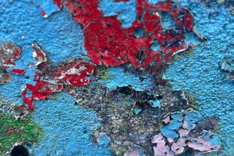A close up of a concrete wall with different colours of pain chipping of