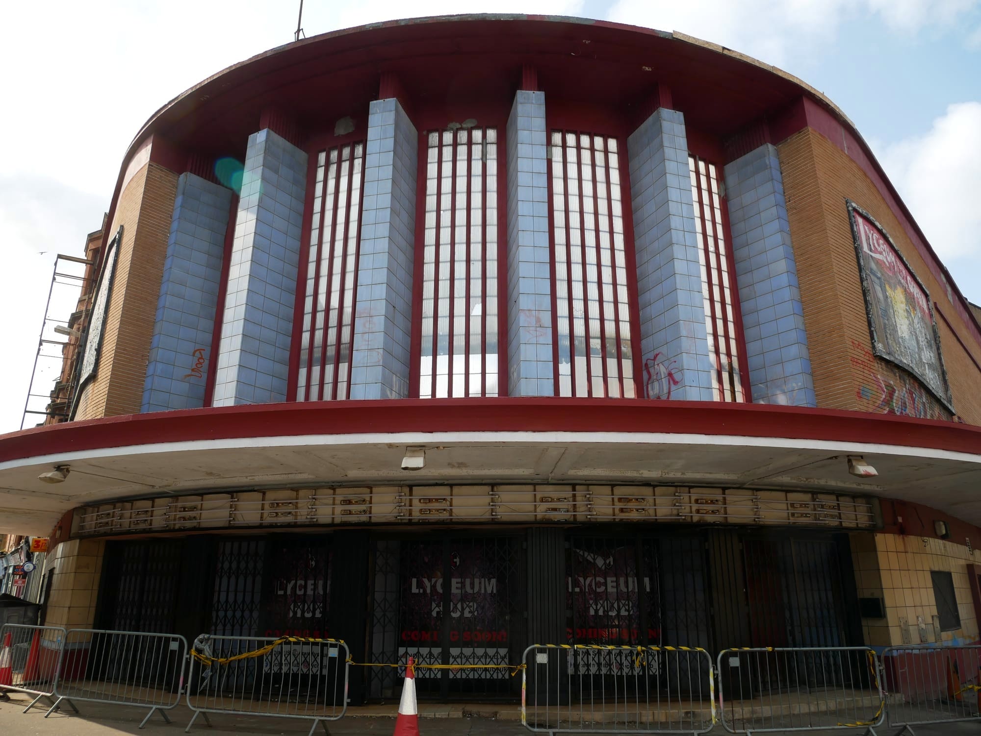 A vacant former cinema photographed from the front. It's a rare example of an International Modern cinema built in the late 1930s. It has blue tiled columns above an awning with reflective glass in between them.