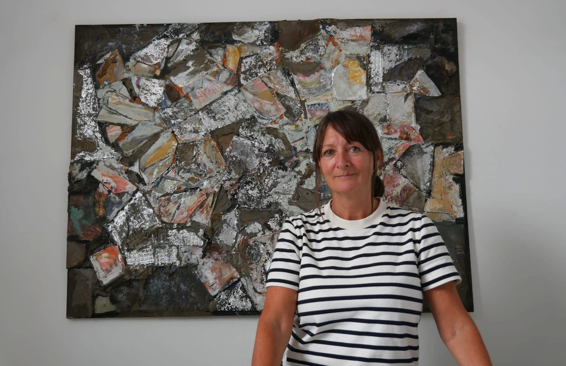 A woman stands in front of an abstract artwork. She's wearing a white tee shirt with black stripes. 