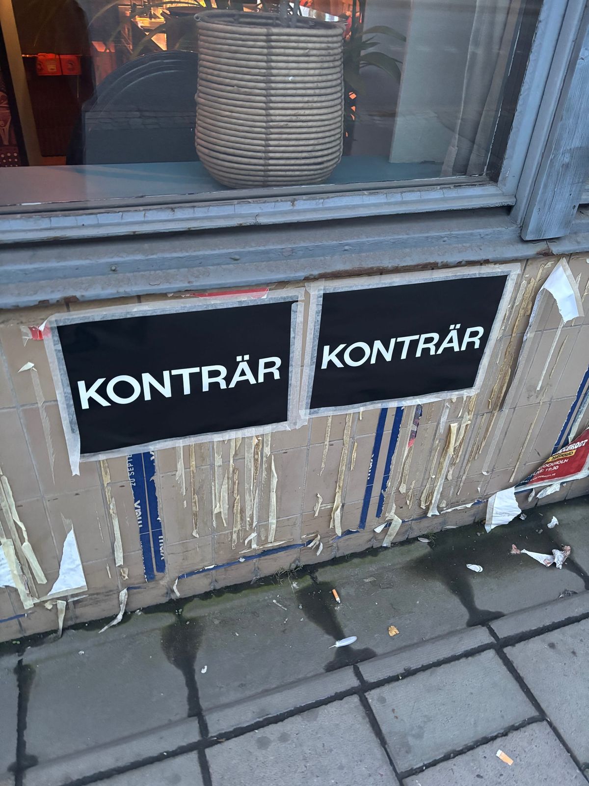 En bild på två affischer med texten KONTRÄR uppsatta på en ostädad gata.