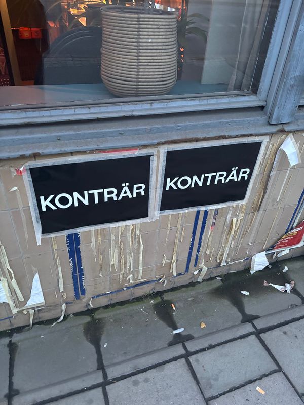 En bild på två affischer med texten KONTRÄR uppsatta på en ostädad gata.