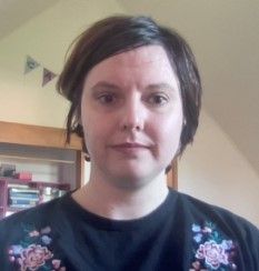 A head and shoulders photo of Amy with short brown hair and books and bunting in the background