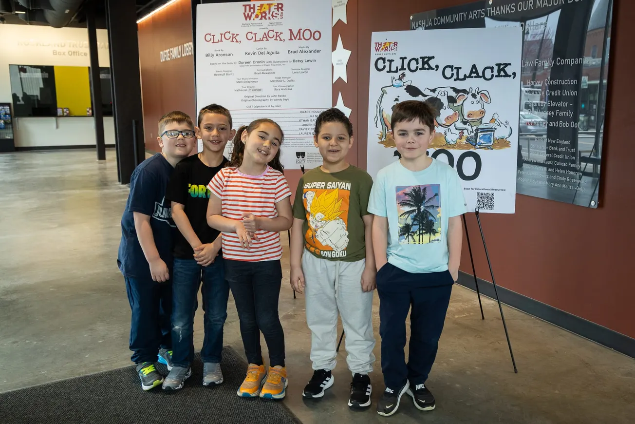 Five elementary school students stand in the Nashua Center for the Arts lobby in front of “Click, Clack, Moo” show posters.