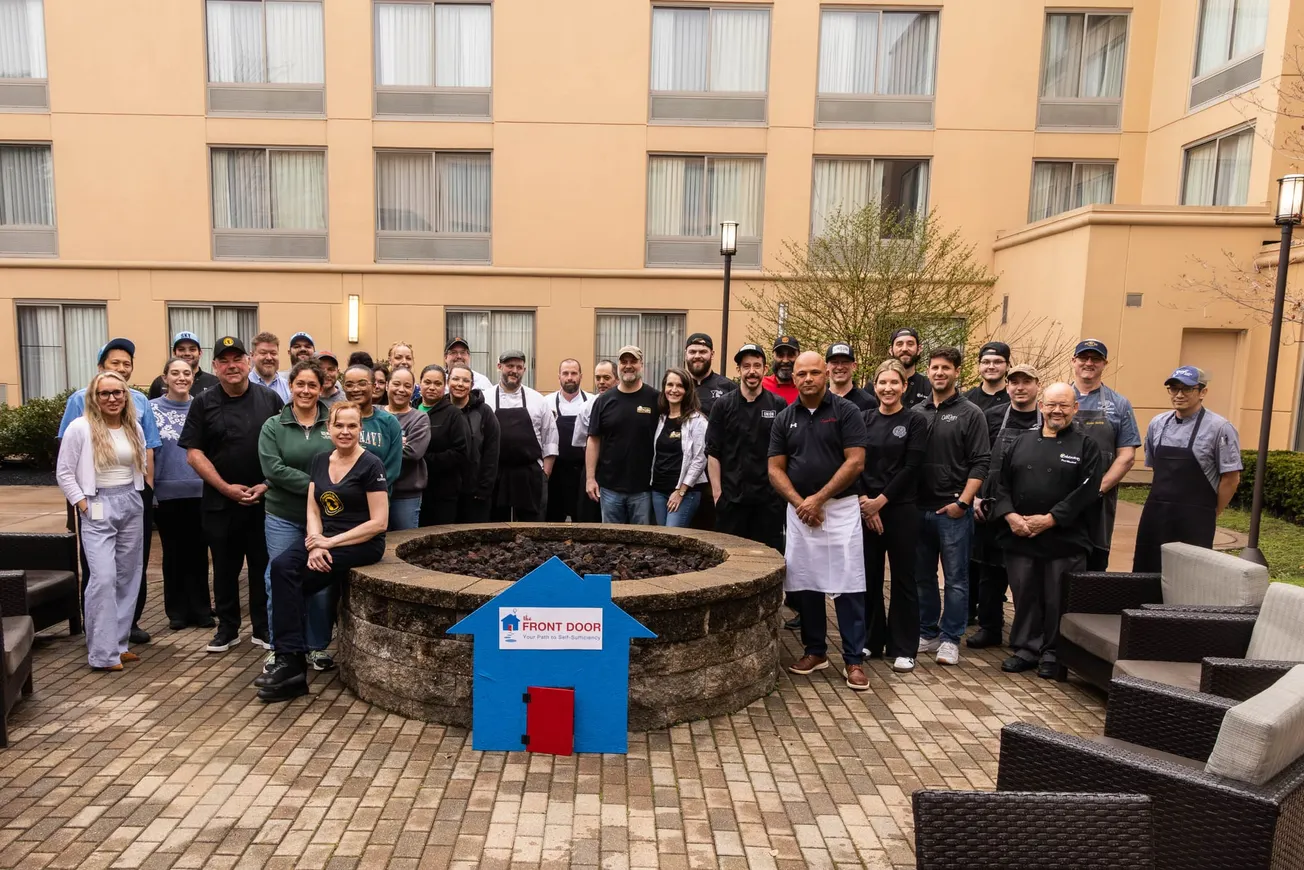Group of restaurant teams stands around an outdoor fire pit with a Front Door Agency sign before the Gourmet Festival and Auction in Nashua, New Hampshire.