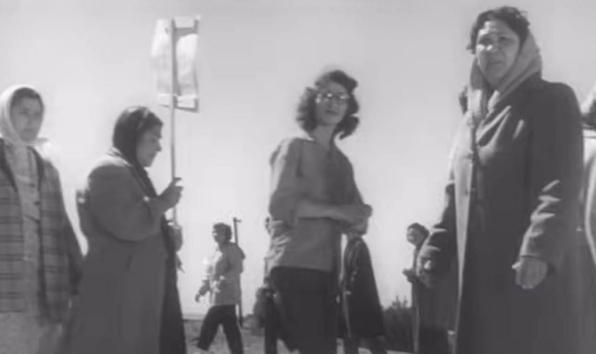 still from the film 'Salt of the Earth'. a circle of women hold signs for the picket line at the entrance to a zinc mine.