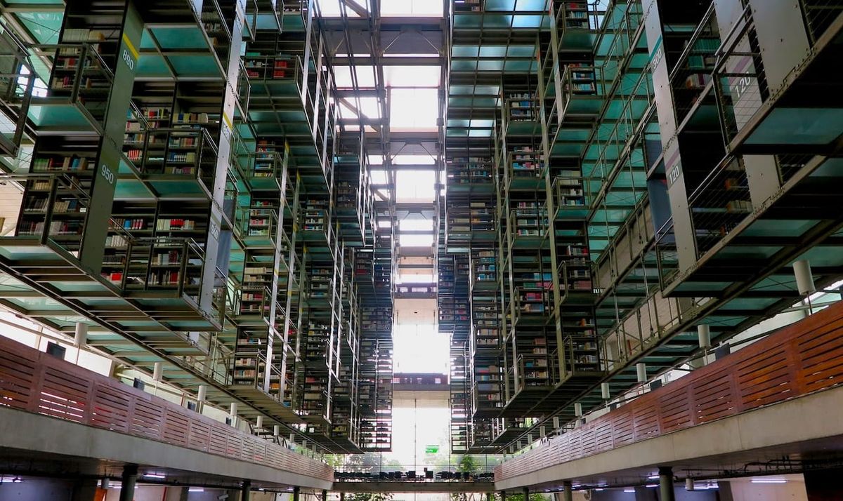 view from the ground floor of biblioteca vasconcelos, a public library in mexico city. shelves of books jut out towards the center of the room.