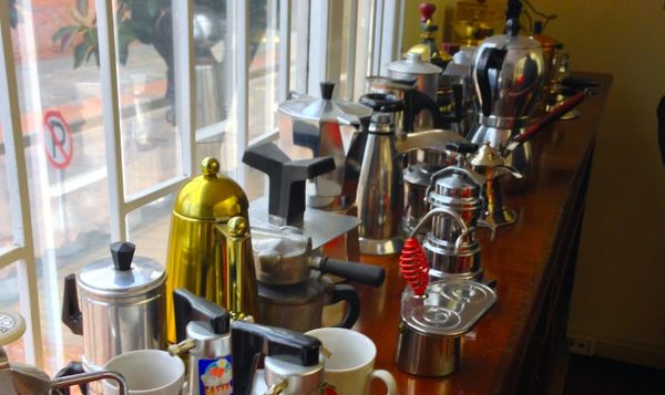 a row of coffee pots and cups line a wooden counter