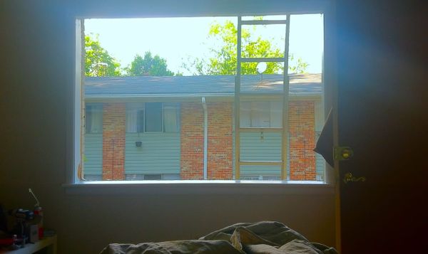 a hole in an exterior wall where a window should be. an open door frames one side of the room while a small table with a bunch of stuff sits on the left.