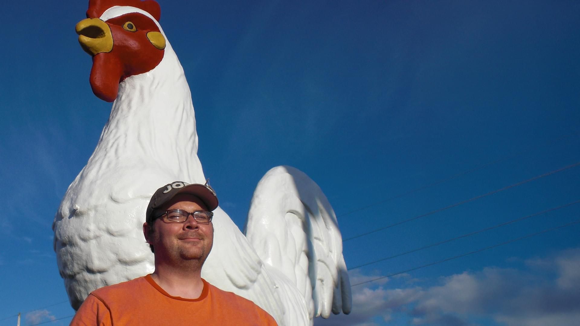 Photo of Jeremy posing in front of a 10-foot tall concrete rooster.