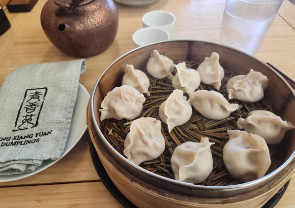A steamer full of dumplings sits on a table with a teapot behind it