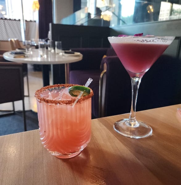 An orange cocktail in a short glass and a purple cocktail in a martini glass