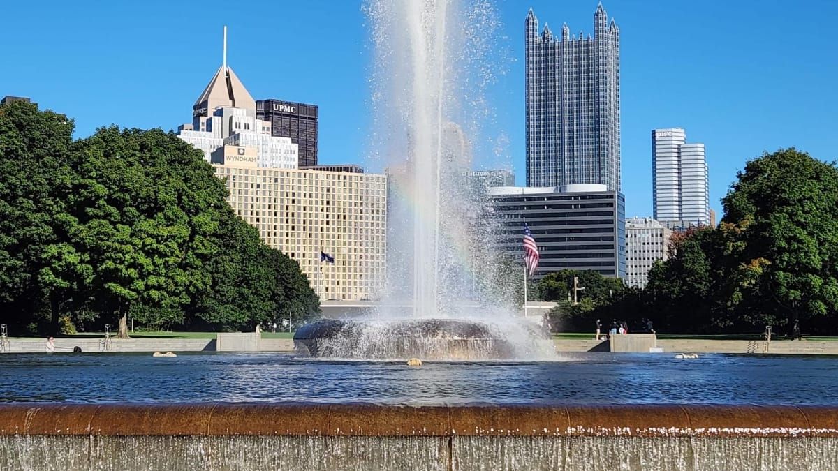 A fountain shoots water in the air with a rainbow shimmering through the water