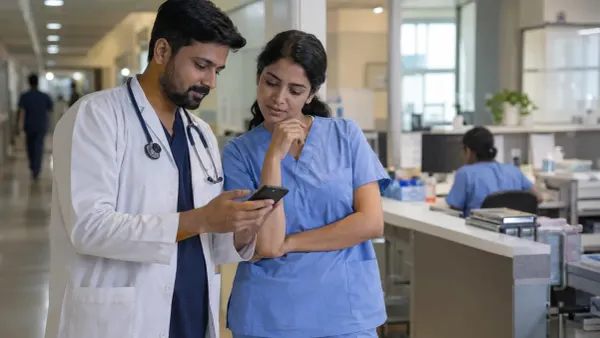 Two healthcare professionals review an unbranded smartphone in a modern hospital corridor, illustrating secure clinical communication.