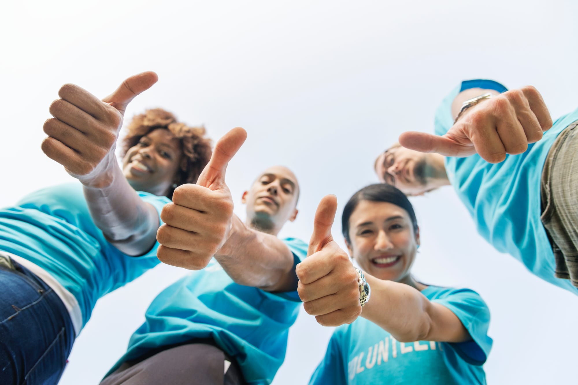 four volunteers in blue shirts giving a thumbs up
