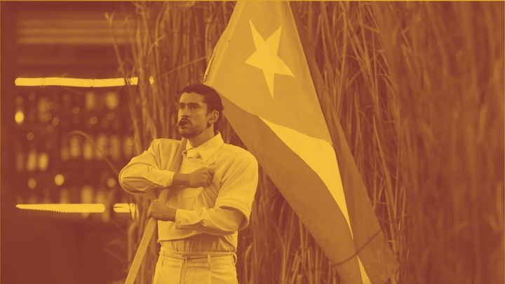 A photo of Bad Bunny from the Super Bowl halftime show. He's holding the Puerto Rican flag and standing in a stance of resistance in his all-white suit.