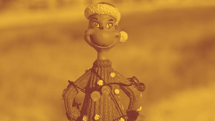 A photo of a smiling Grinch figurine wrapped in Christmas lights. He looks happy but a little cranky.