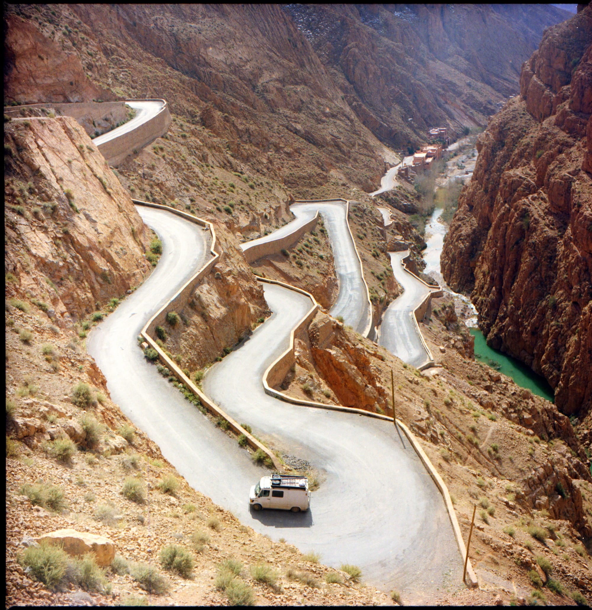 A winding road with multiple switchbacks descending through a rocky canyon, with a van driving down the road.
