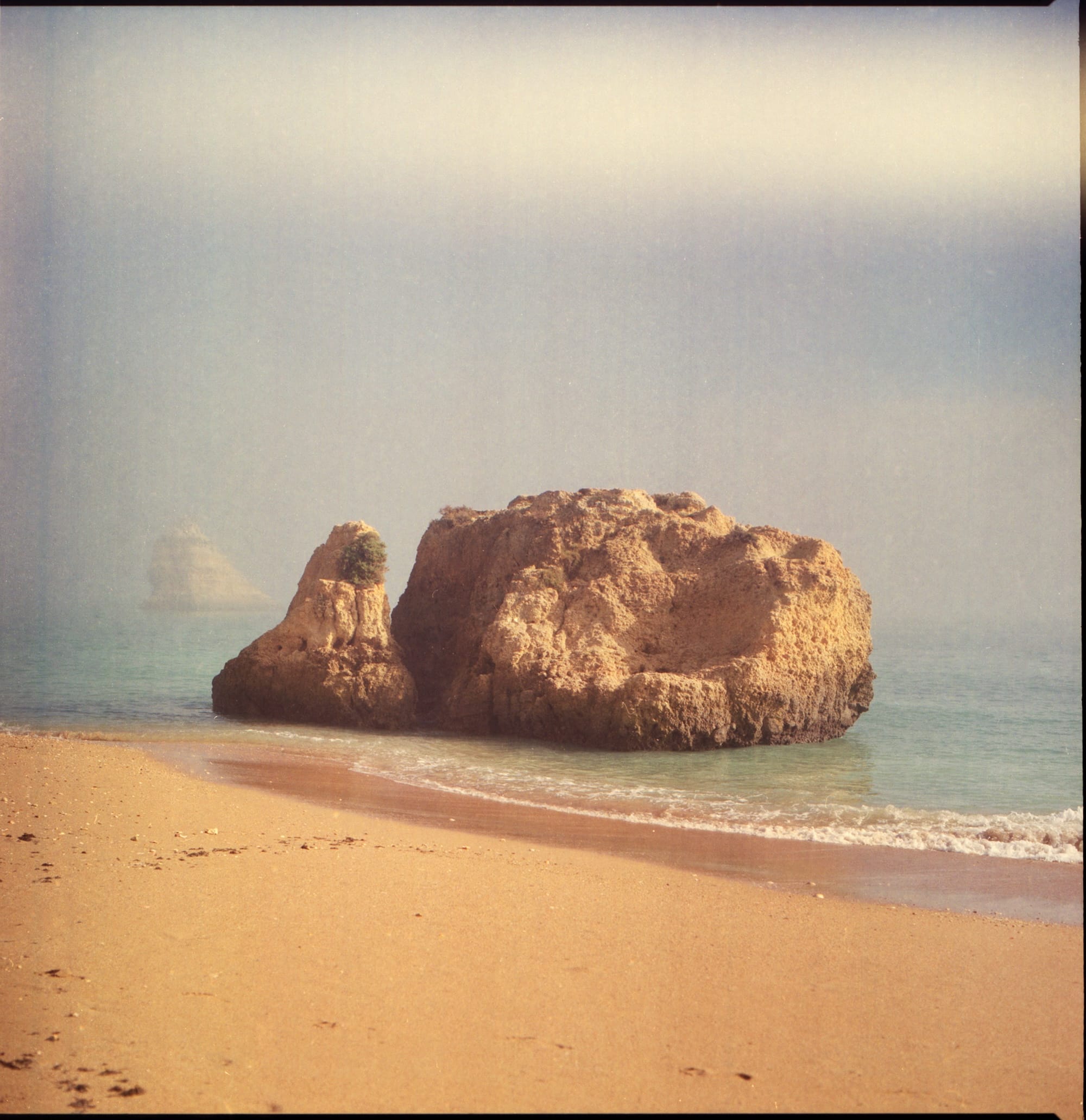 A large rock formation on a sandy beach with the ocean in the background.