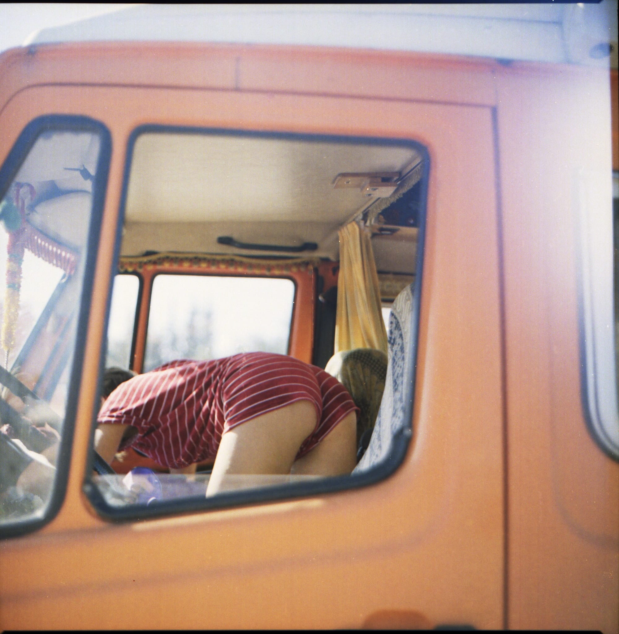 Interior view of a van through an open window, showing a young woman bending over to organize supplies.