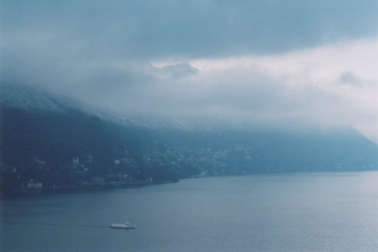Serene sea view with a boat on calm waters and misty mountains in the background.