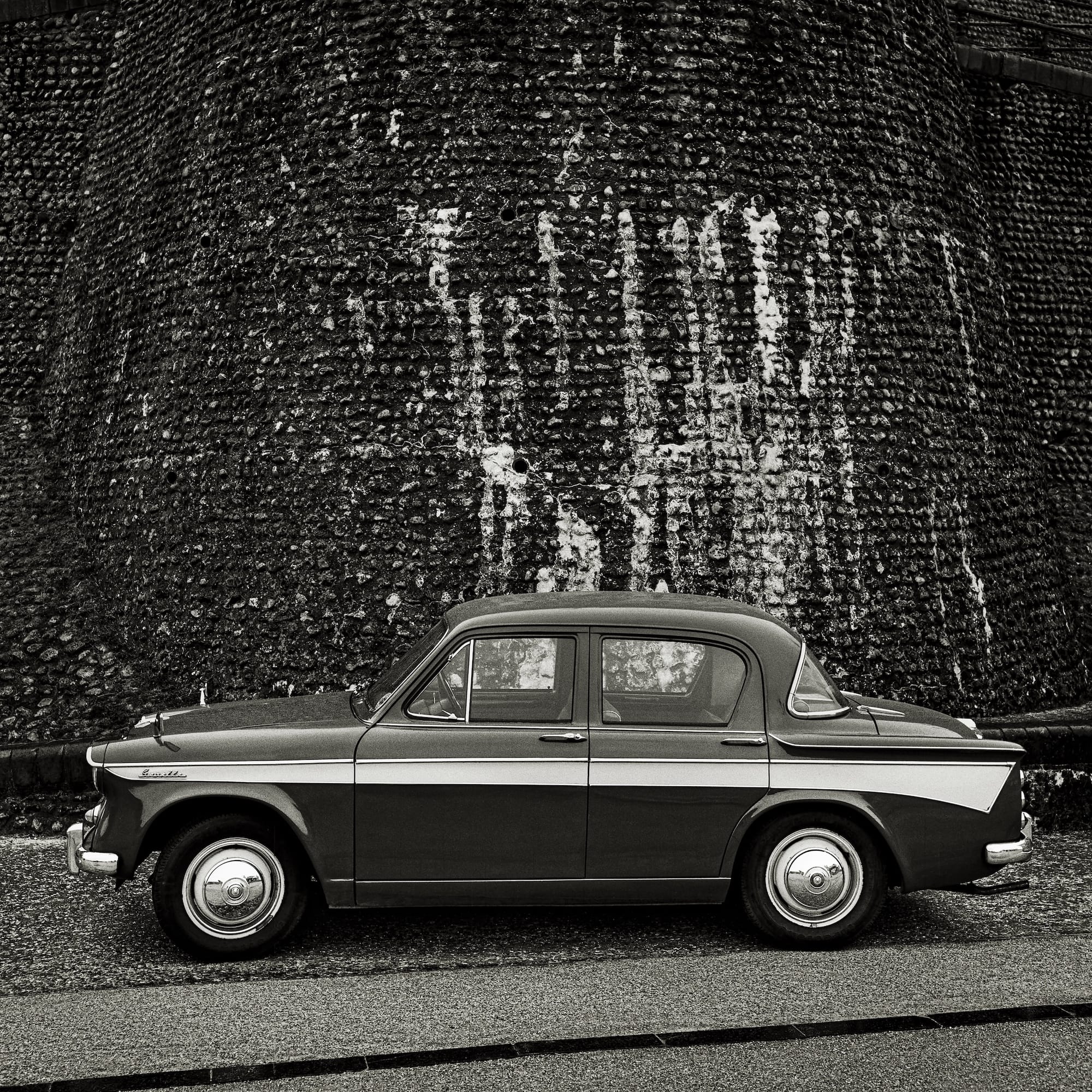 Vintage automobile with chrome details, parked against a textured stone wall.