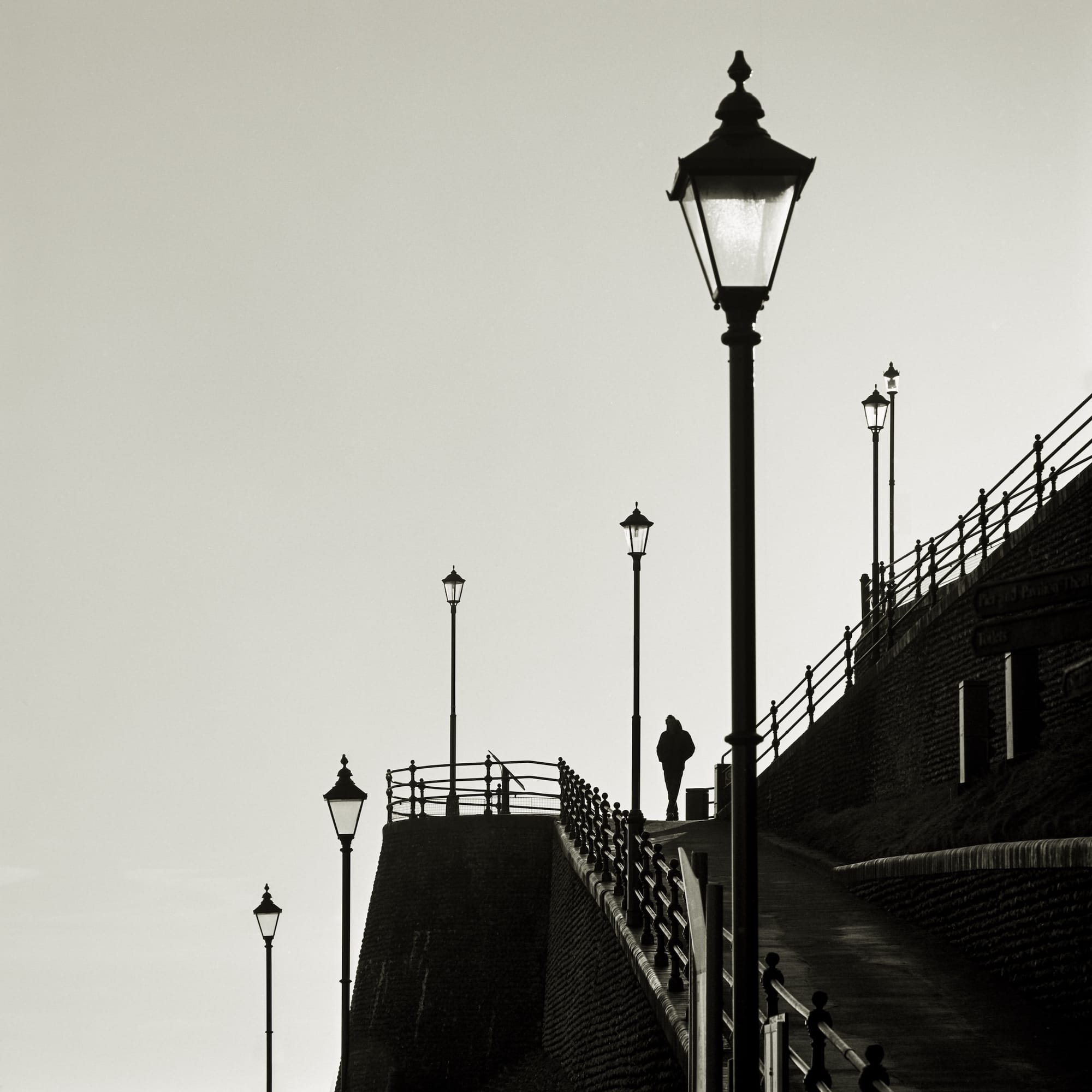 Vintage street lamps along the Cromer coast, with a solitary figure walking in the distance.