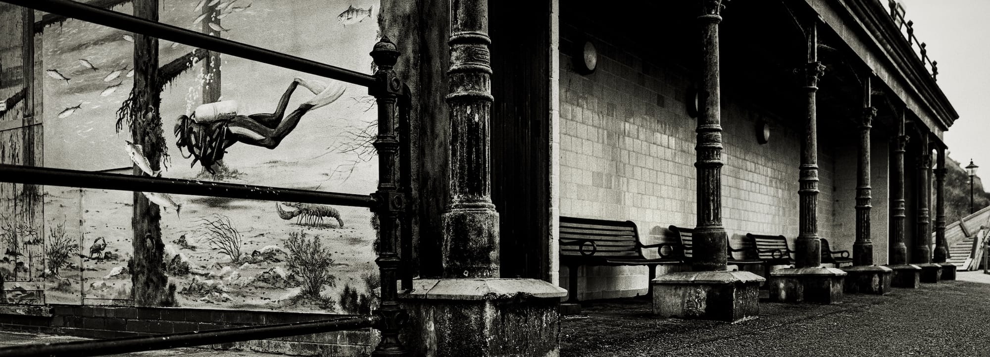 Black and white photo of a row of vintage lampposts and benches in a covered walkway.